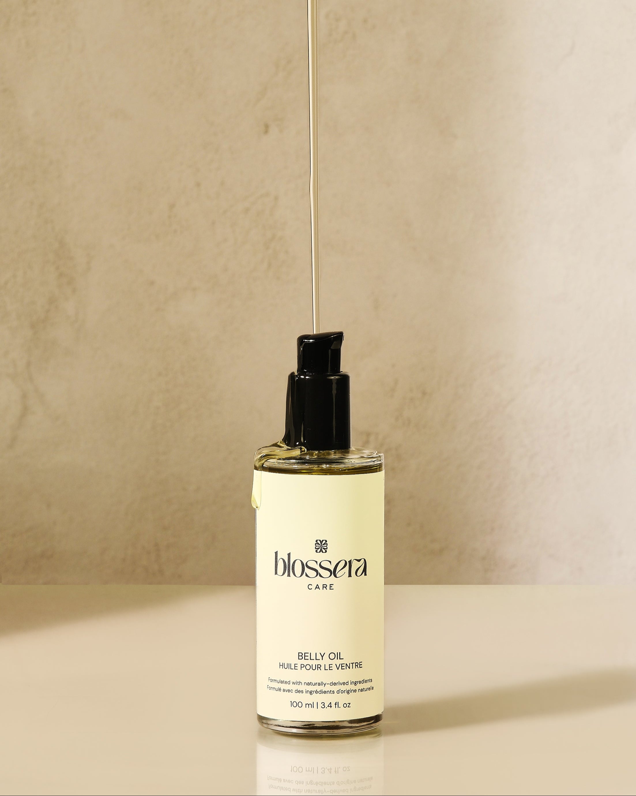 Aesthetic product shot of Blossera Belly Oil with oil dripping to show lightweight, nourishing texture.