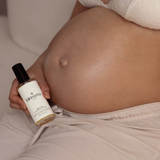 Pregnant person holding Blossera Belly Oil bottle next to baby bump for daily belly care
