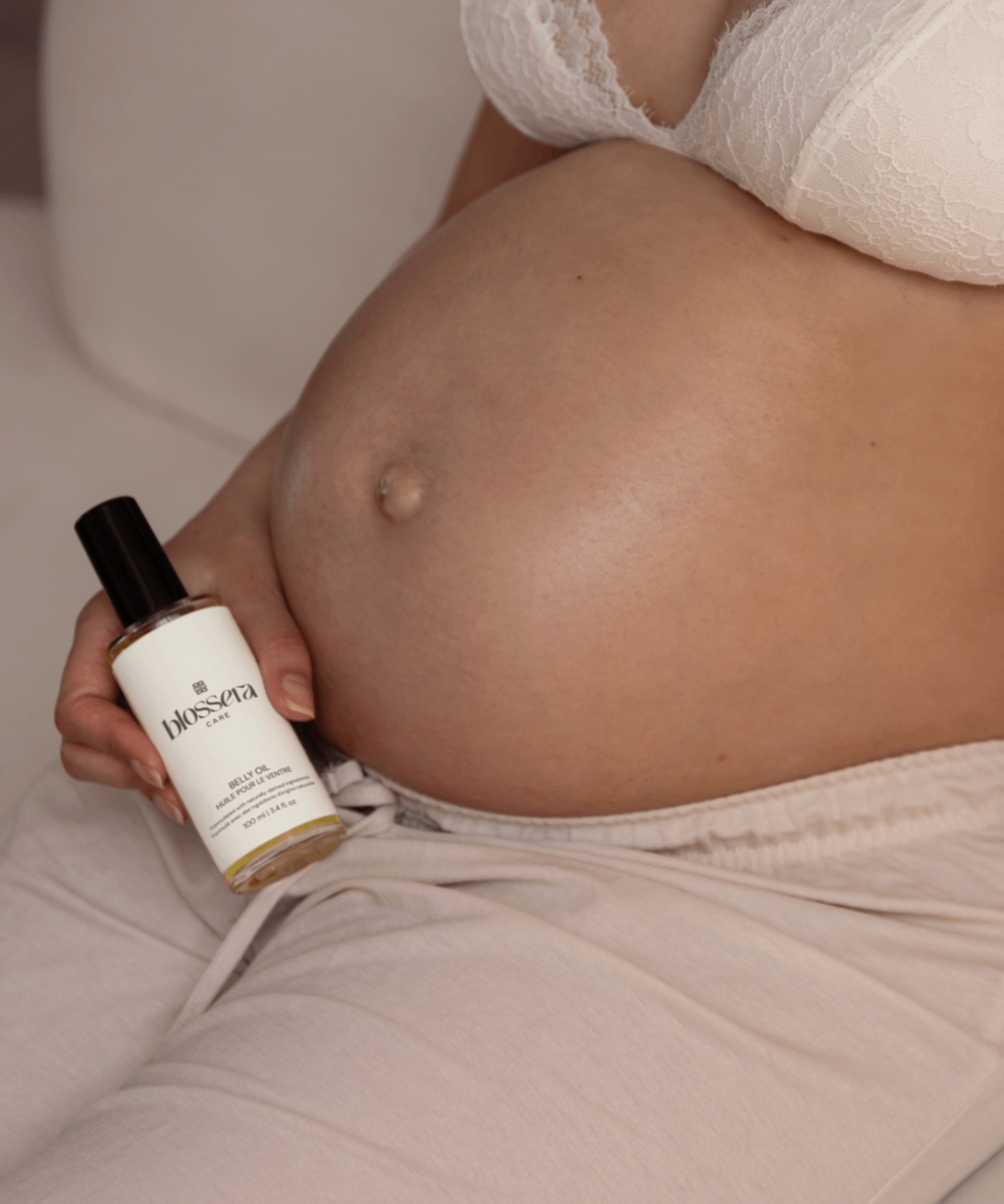 Pregnant person holding Blossera Belly Oil bottle next to baby bump for daily belly care