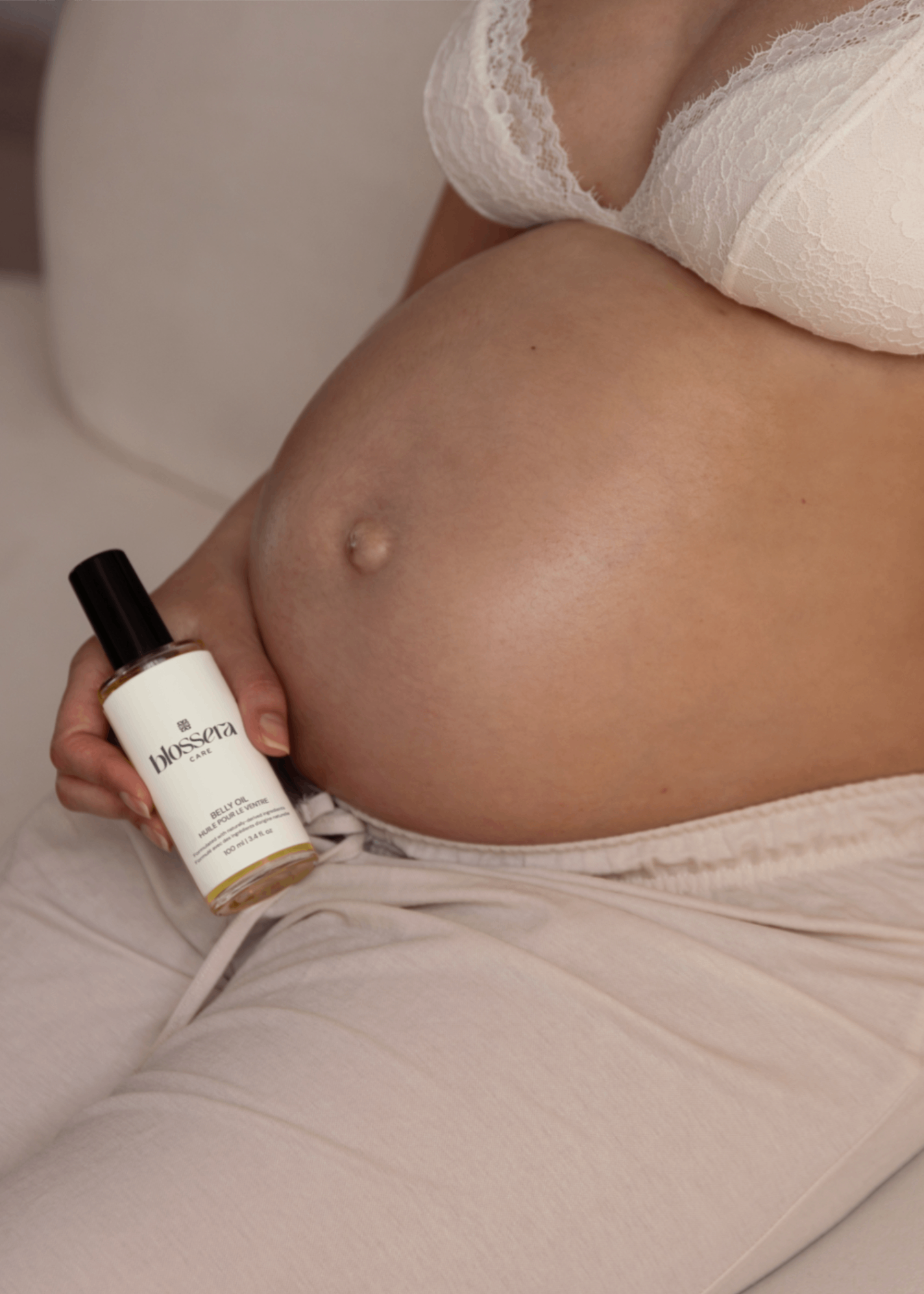 Pregnant person holding Blossera Belly Oil bottle next to baby bump for daily belly care